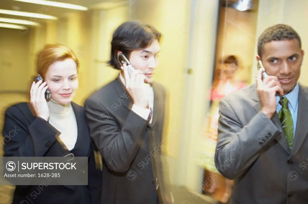 Close-up of two businessmen with a businesswoman talking on mobile phones