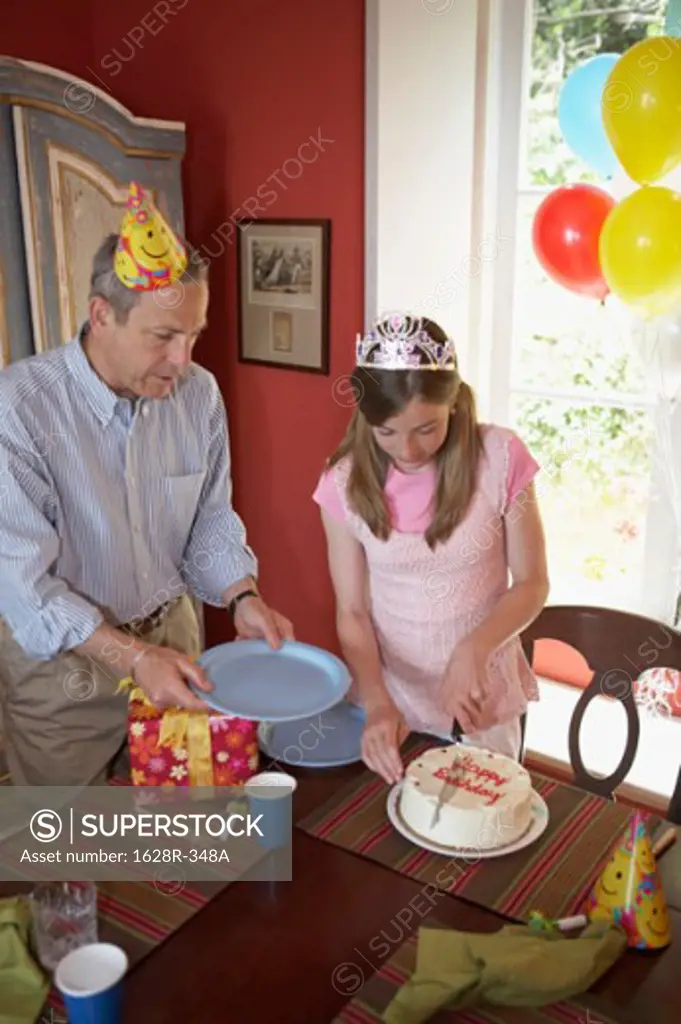 High angle view of a teenage girl cutting a birthday cake with her grandfather standing near her