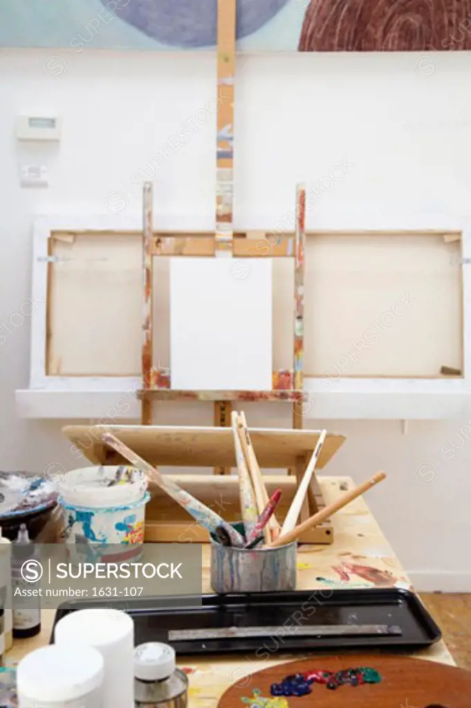 Paintbrushes with paint cans and a drawing board on a table