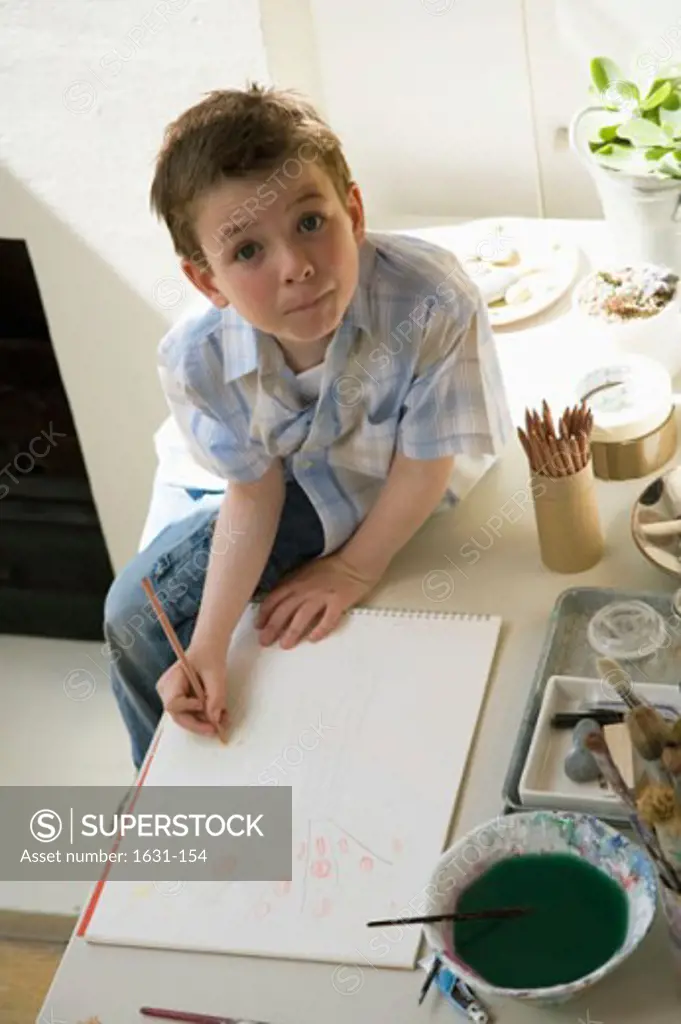 Portrait of a boy sitting on a table and drawing on a sketch pad