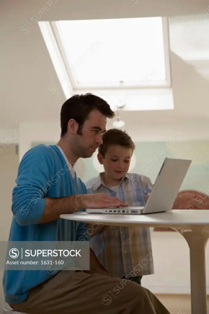 Side profile of a young man using a laptop with his son standing beside him