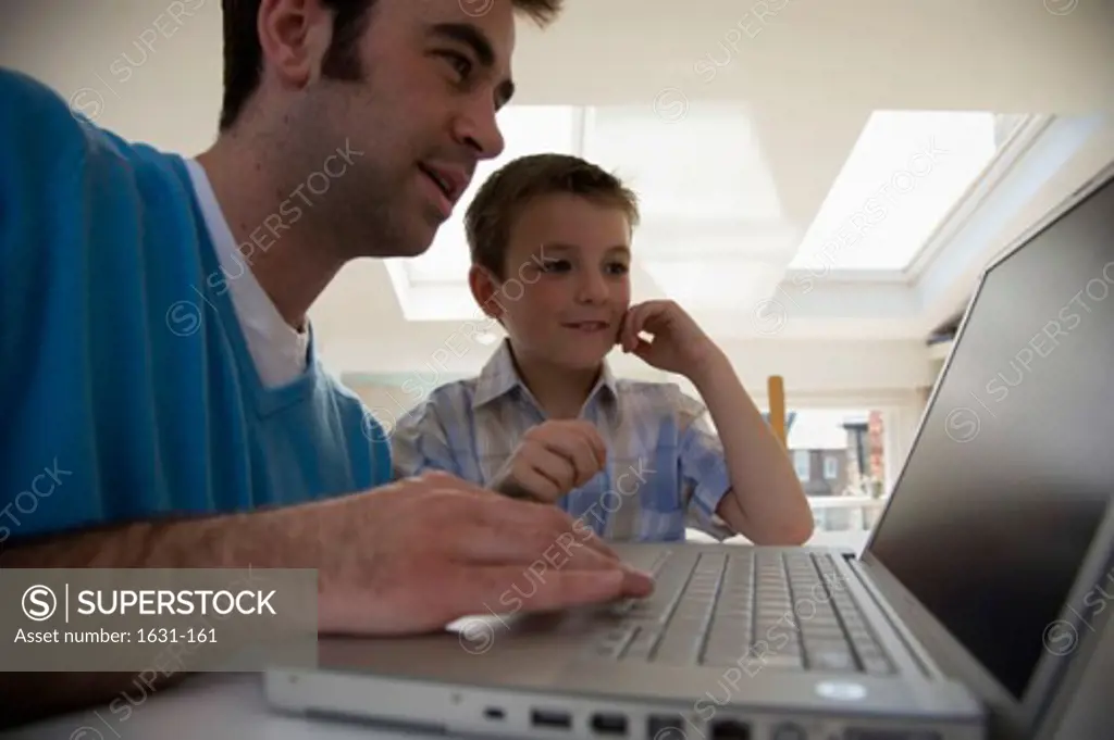 Close-up of a young man using a laptop with his son standing beside him