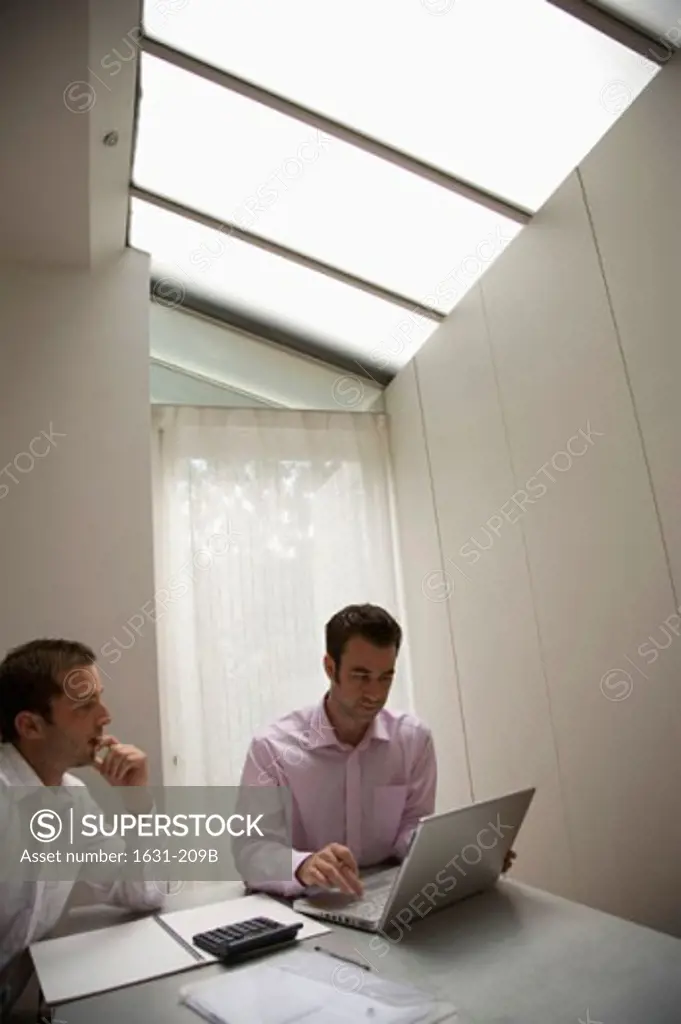 Businessman using a laptop with another businessman sitting beside him