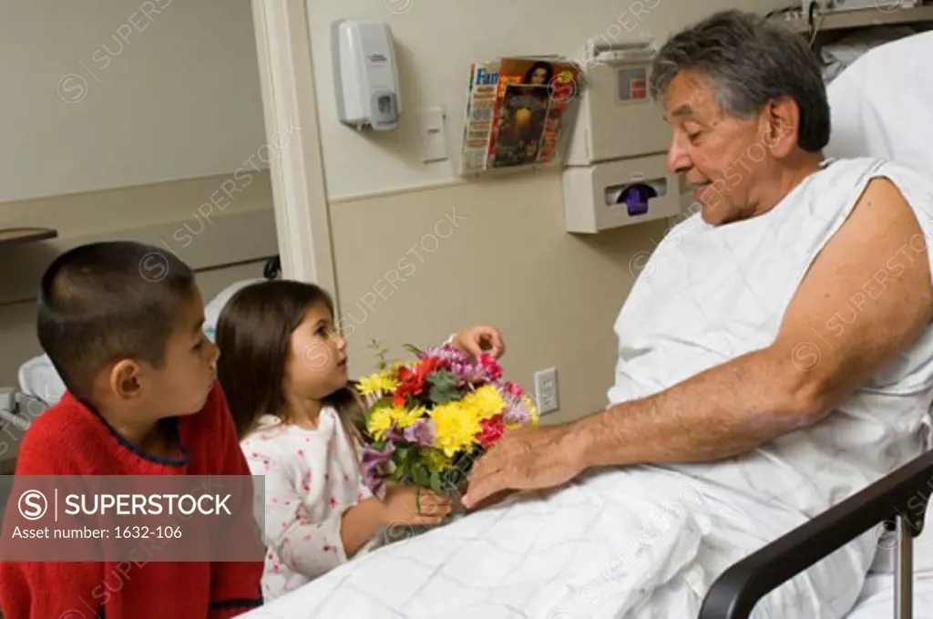 Close-up of a girl and her brother giving a bouquet of flowers to their grandfather