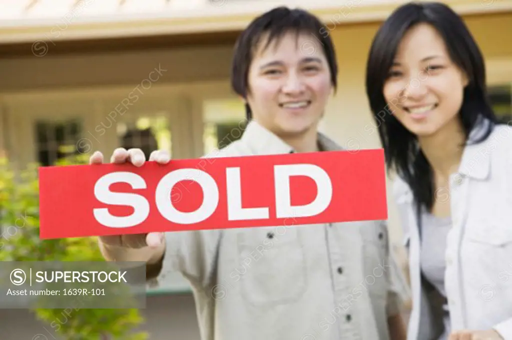 Portrait of a young man holding a sold sign with a young woman standing beside him