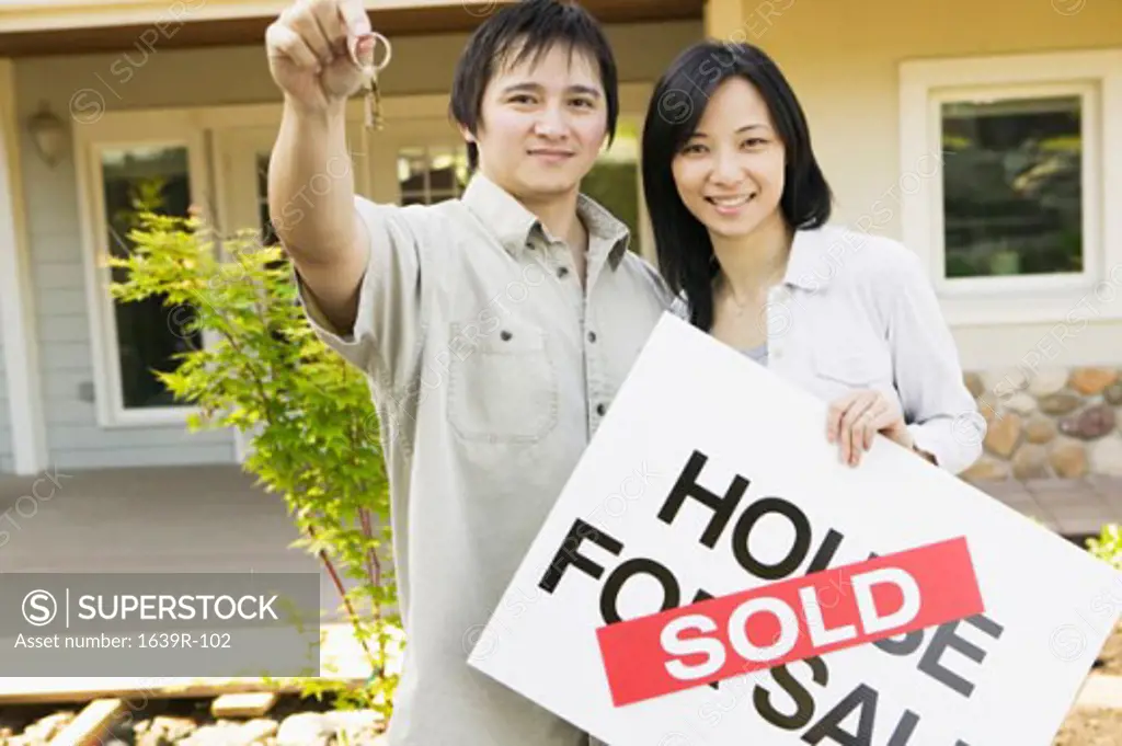 Portrait of a young woman holding a sold sign with a young man holding keys