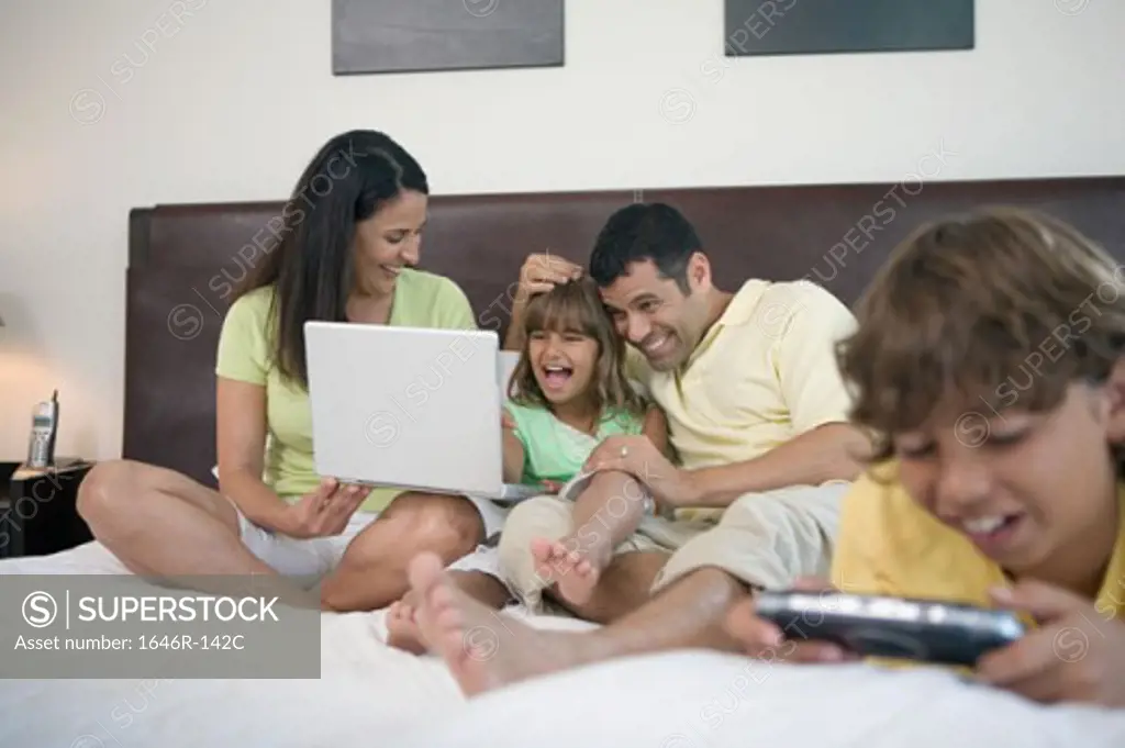 Close-up of a boy playing a video game in the bed and his parents and sister behind him