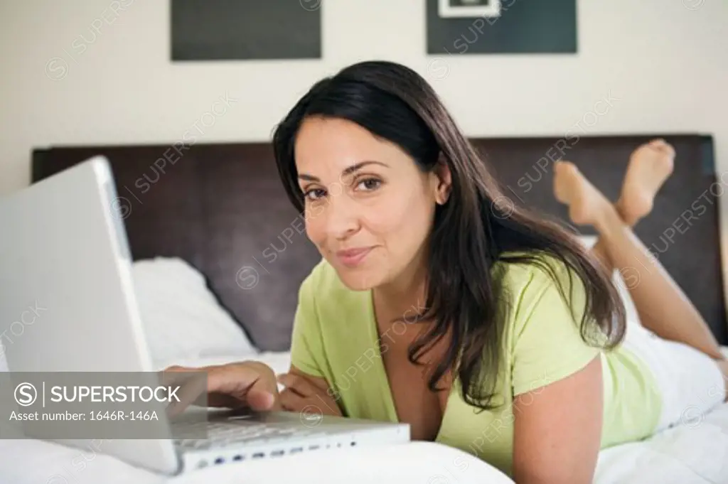 Portrait of a mature woman lying in the bed and using a laptop