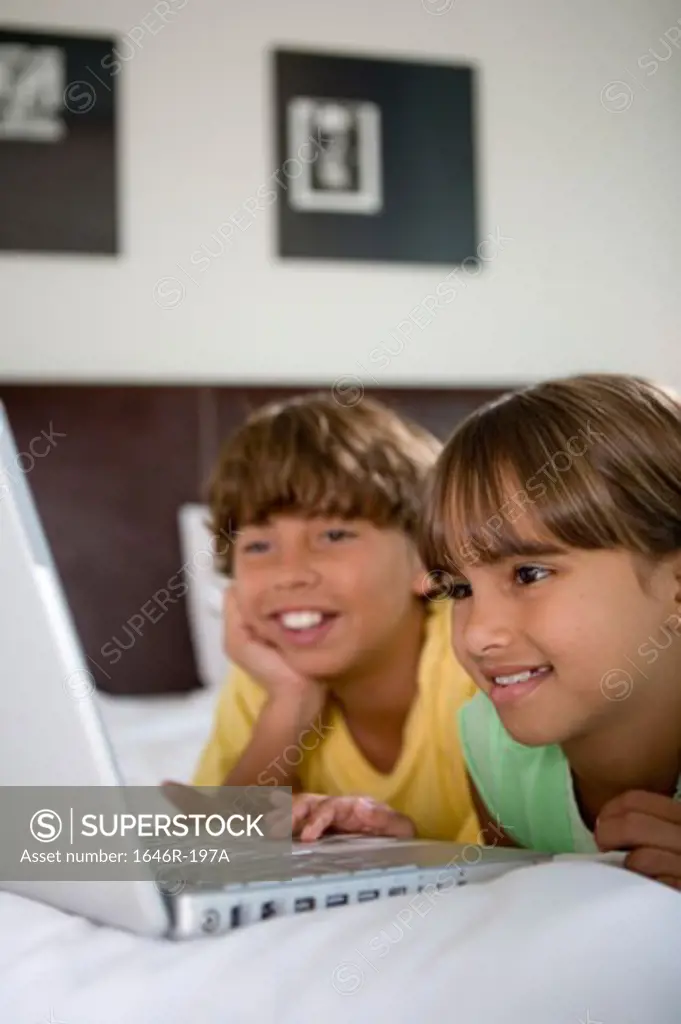 Close-up of a girl lying in the bed with her brother using a laptop