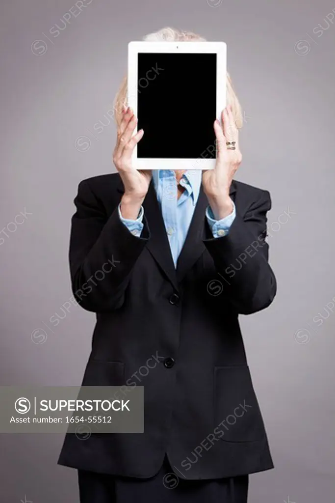 Studio. Senior businesswoman holding tablet up to her face showing another face on her tablet