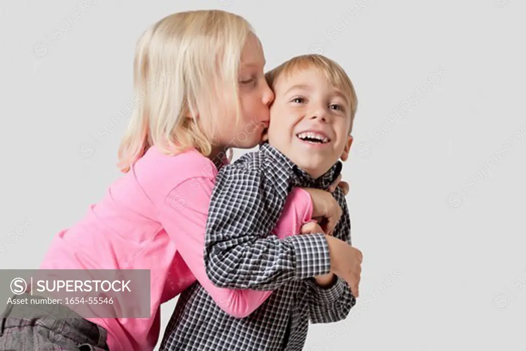 Studio. Young girl kissing and embracing brother over white background