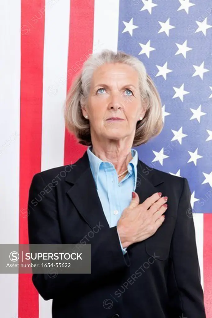 Studio. Senior businesswoman with hand over heart against American flag