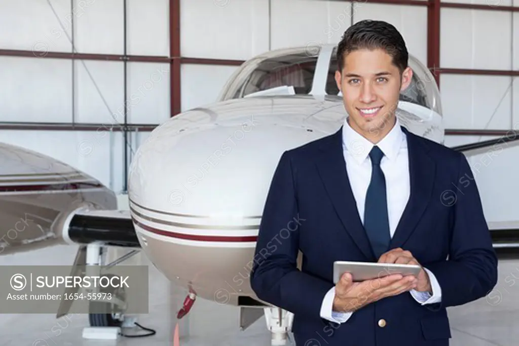 Palm Springs, California, USA. Portrait of handsome young pilot using tablet PC in front of airplane