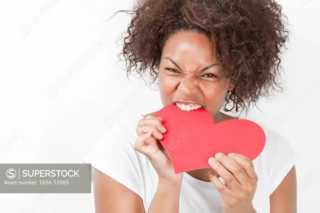 London, UK. Portrait of frustrated young African American woman biting heart shape against white background