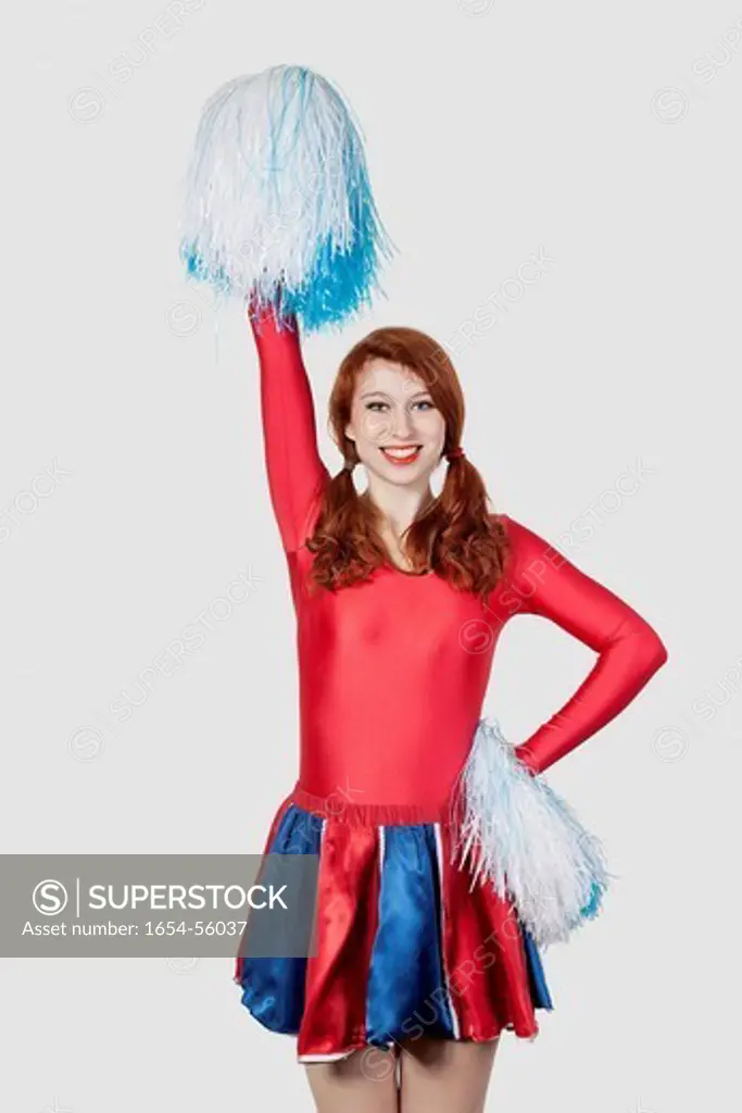 London, UK. Portrait of happy young woman in cheer leader costume standing against gray background