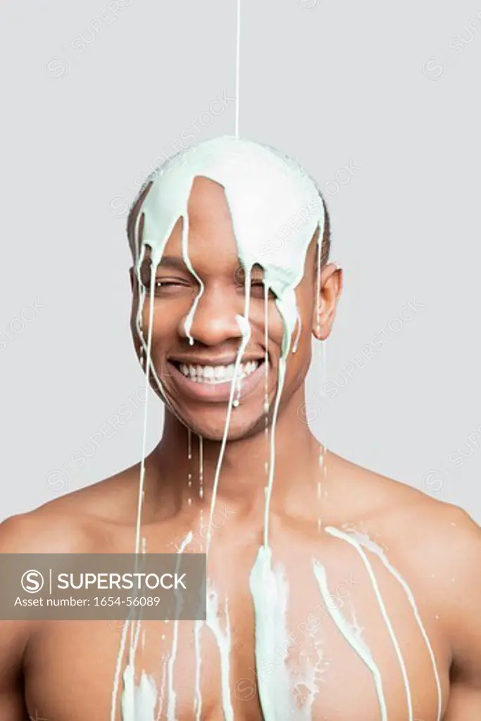 London, UK. Shirtless young man with paint falling on his head against gray background