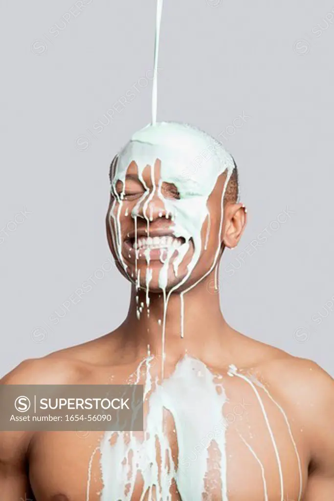 London, UK. Paint falling on happy shirtless young man´s head against gray background