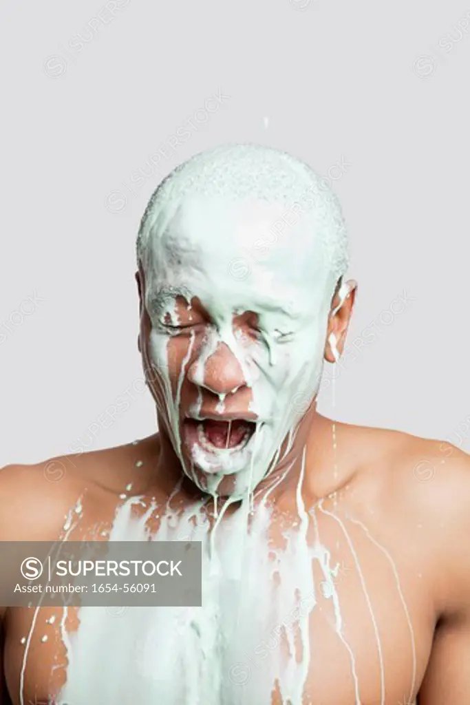 London, UK. Shirtless young man covered in paint with mouth open against gray background