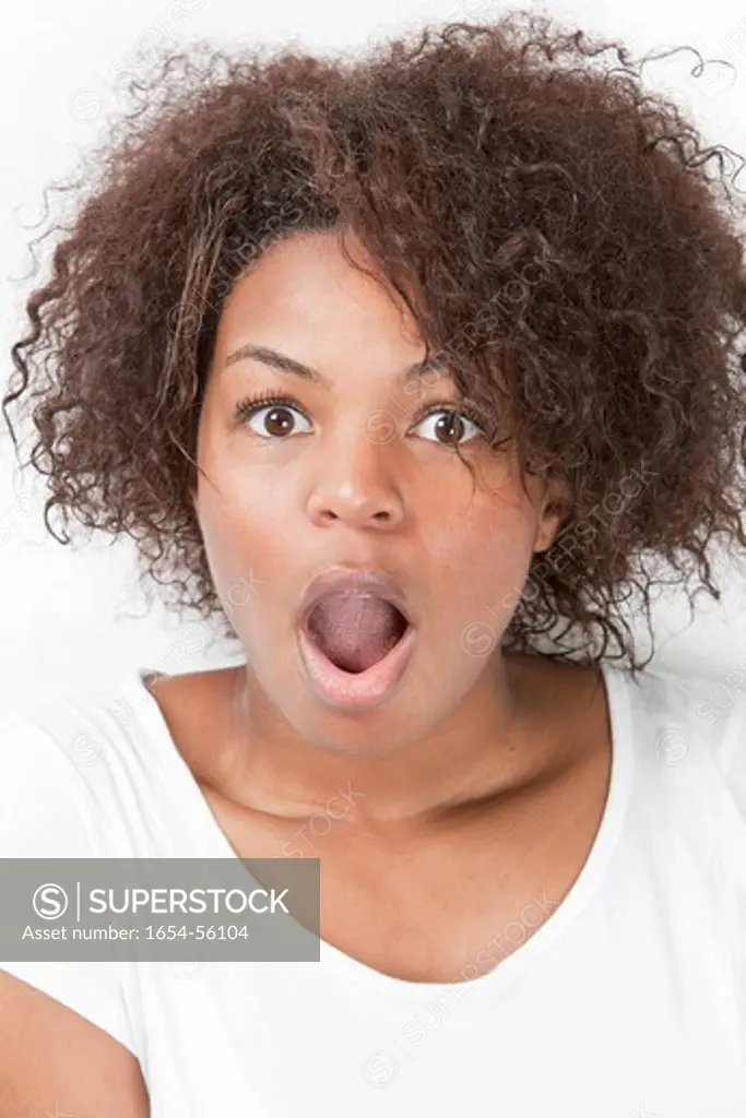 London, UK. Portrait of shocked young woman with mouth open against white background