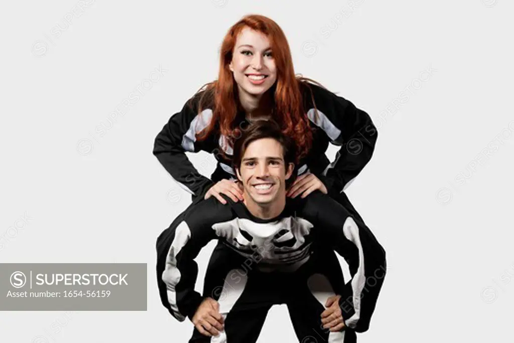 London, UK. Portrait of young man giving piggyback ride in skeleton costume over gray background