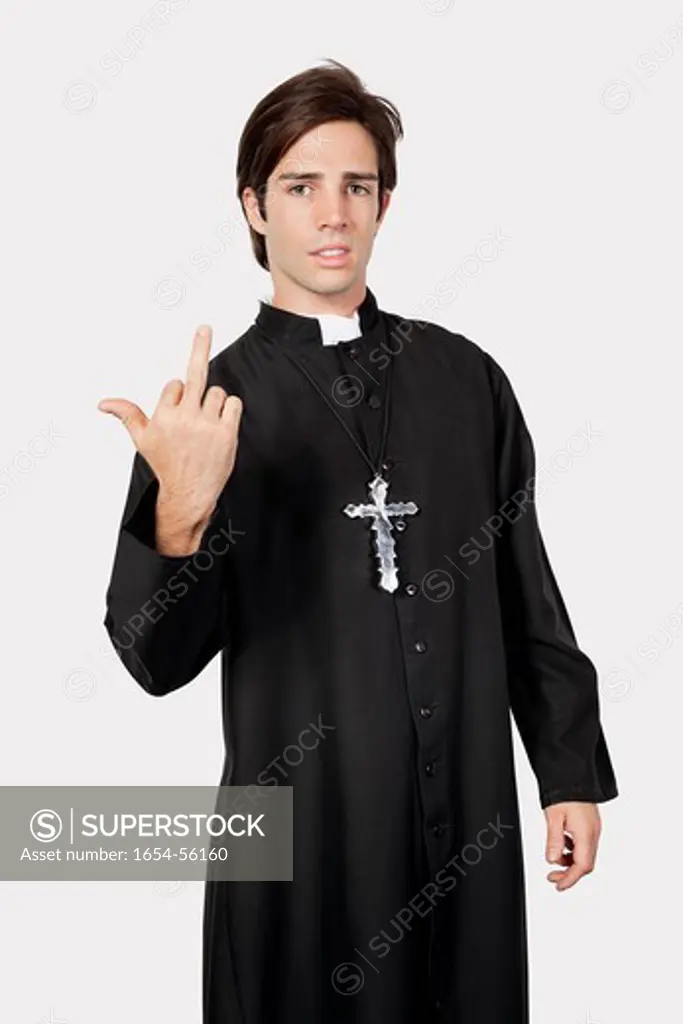 London, UK. Portrait of young man in priest costume with rude gesture against gray background