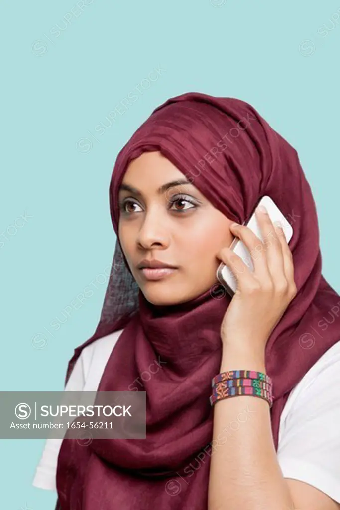 London, UK. Young Muslim woman in maroon headcloth using cell phone against blue background