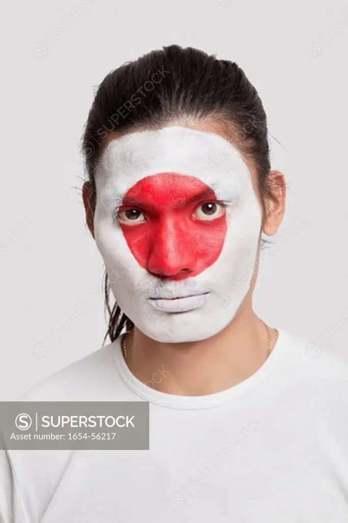 London, UK. Portrait of serious young mixed race man with Japanese flag painted on face against white background