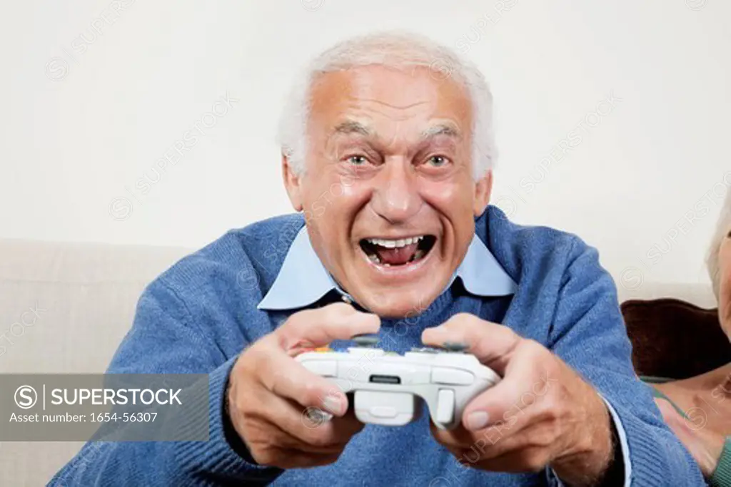 London, UK. Portrait of excited elderly man playing video game at home