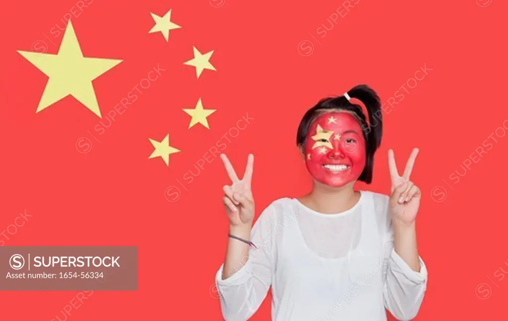 London, UK. Portrait of young Asian woman with painted face gesturing peace sign against Chinese flag