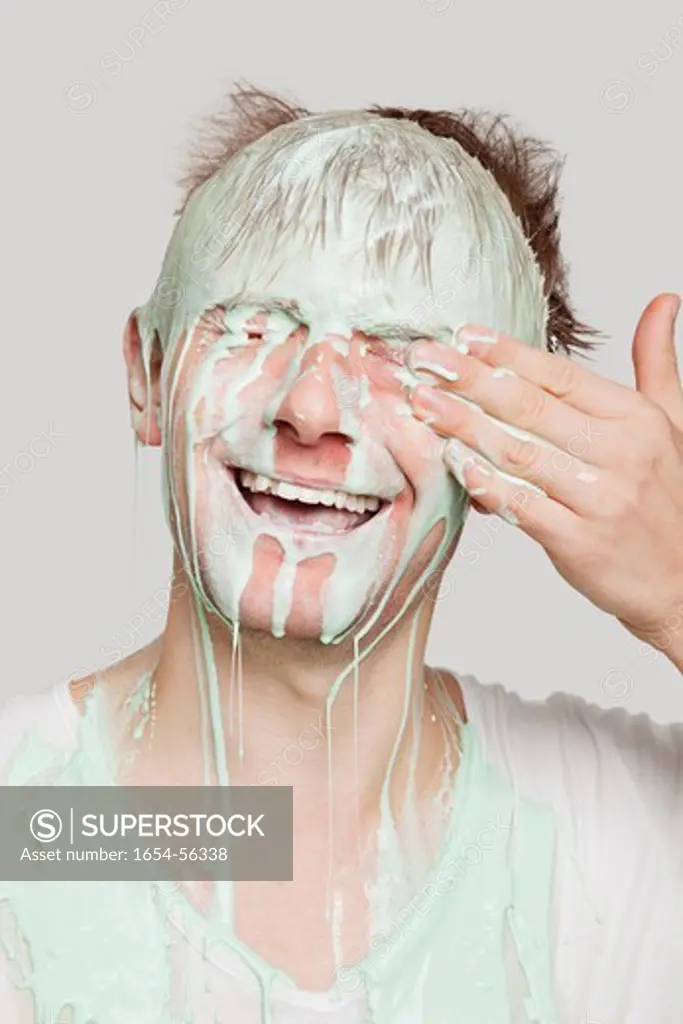 London, UK. Young Caucasian man covered with paint wiping his eyes against gray background