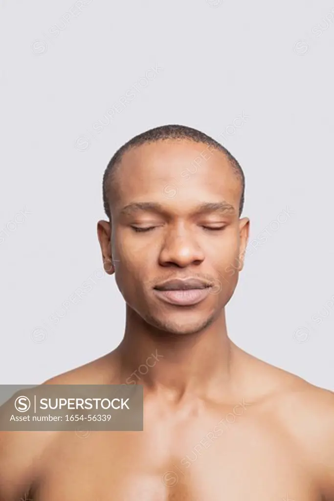 London, UK. Young shirtless man with eyes closed against gray background