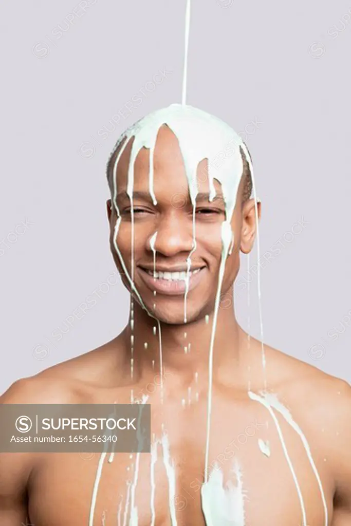 London, UK. Portrait of shirtless young man with paint falling on his head against gray background