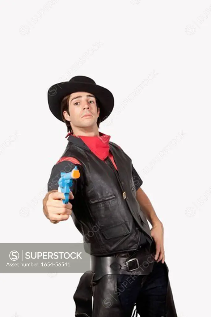 London, UK. Portrait of young cowboy aiming handgun against gray background