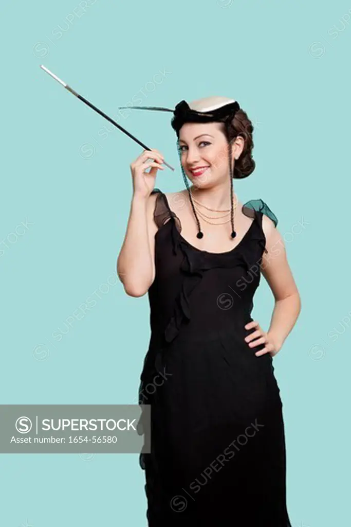 London, UK. Portrait of happy young woman in black dress holding old_fashioned cigarette holder against blue background