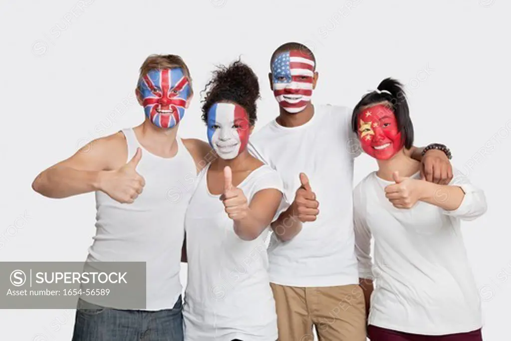 London, UK. Portrait of happy Multi_ethnic group of friends with various national flags painted on their faces gesturing thumbs up against white background