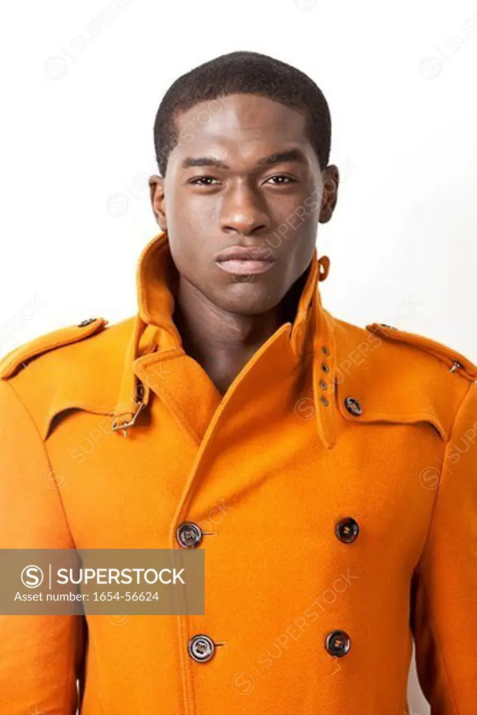 London, UK. Portrait of confident young man in orange trench coat against white background