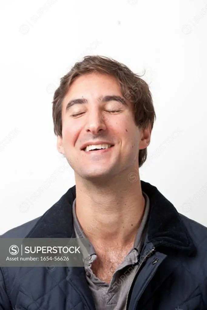 London, UK. Close_up of young man with eyes closed smiling against white background