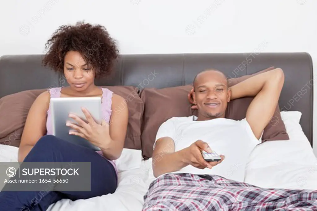 London, UK. Young man watching TV while woman using tablet PC in bed