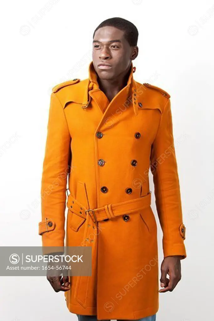London, UK. Young African American man in orange trench coat standing against white background
