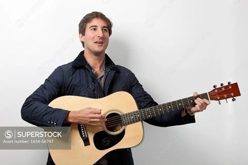 London, UK. Young man playing guitar while signing against white background