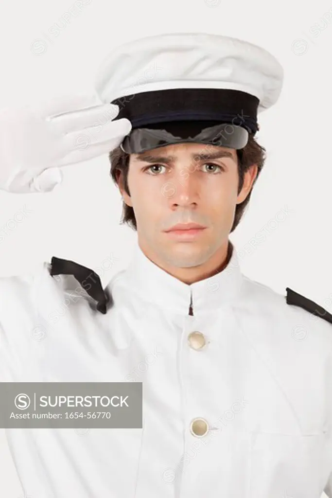 London, UK. Portrait of young navy officer saluting against gray background