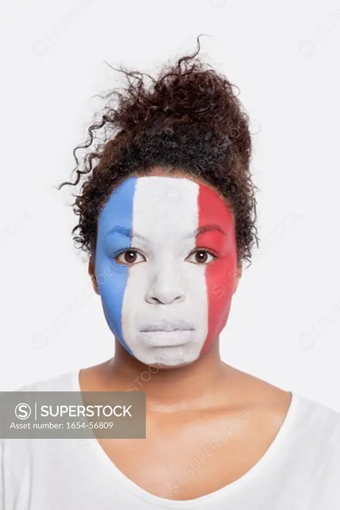 London, UK. Portrait of sad young African American woman with French flag painted on face against white background