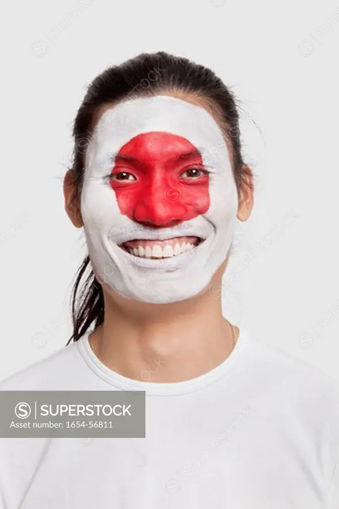 London, UK. Portrait of happy young mixed race man with Japanese flag painted on face against white background