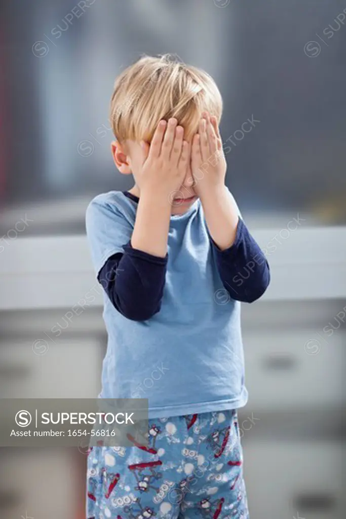 London, UK. Scared little boy in casuals with hands over his eyes