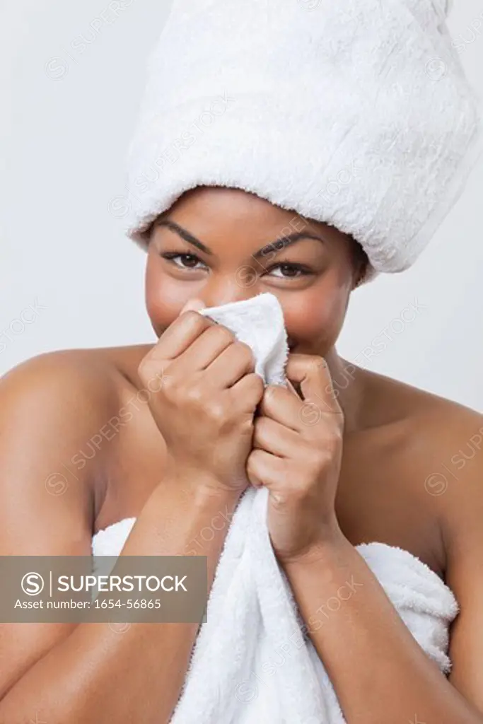 London, UK. Portrait of smiling young African American woman wrapped in towel over white background