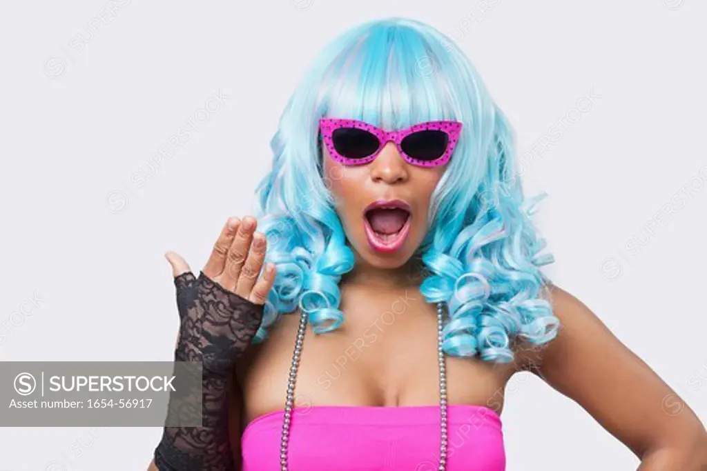London, UK. Portrait of surprised African American woman in blue wig over white background