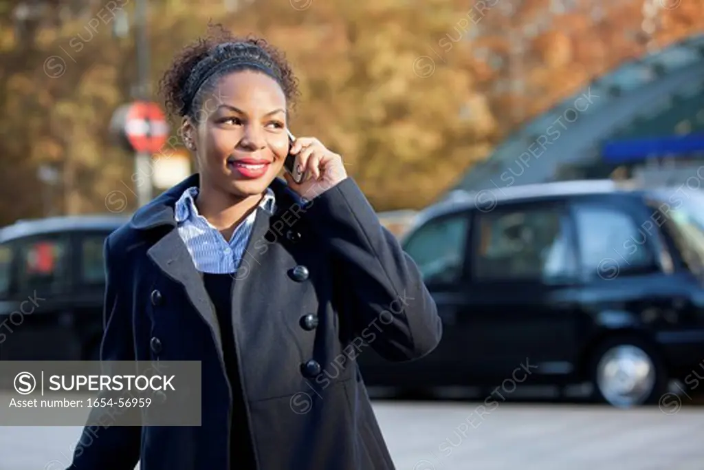 London, UK. Smiling African American young woman using mobile phone outdoors
