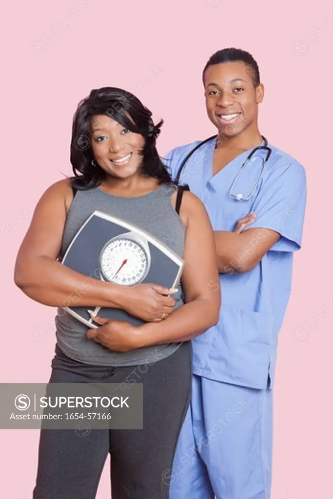 London, UK. Overweight mixed race woman holding scales over pink background