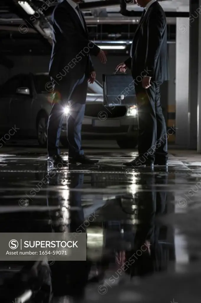 Low section of businessmen giving and receiving briefcase in parking lot