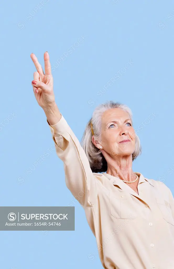 Senior woman in casuals gesturing peace sign against blue background